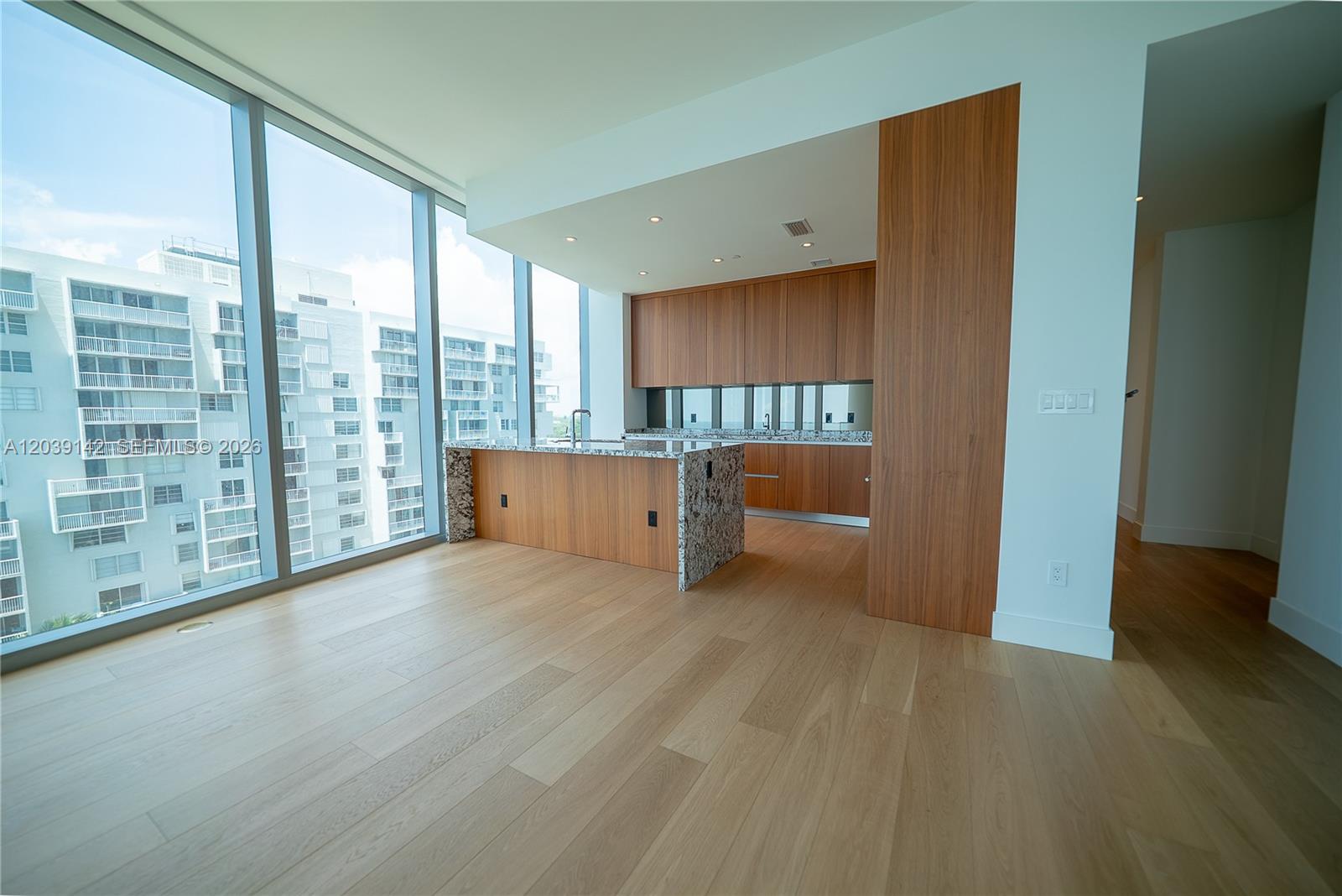 A modern kitchen with wood cabinetry and granite countertops overlooks a city view through windows — 175 SE 25th Rd # 702, Miami FL 33129, MIAMI, FL