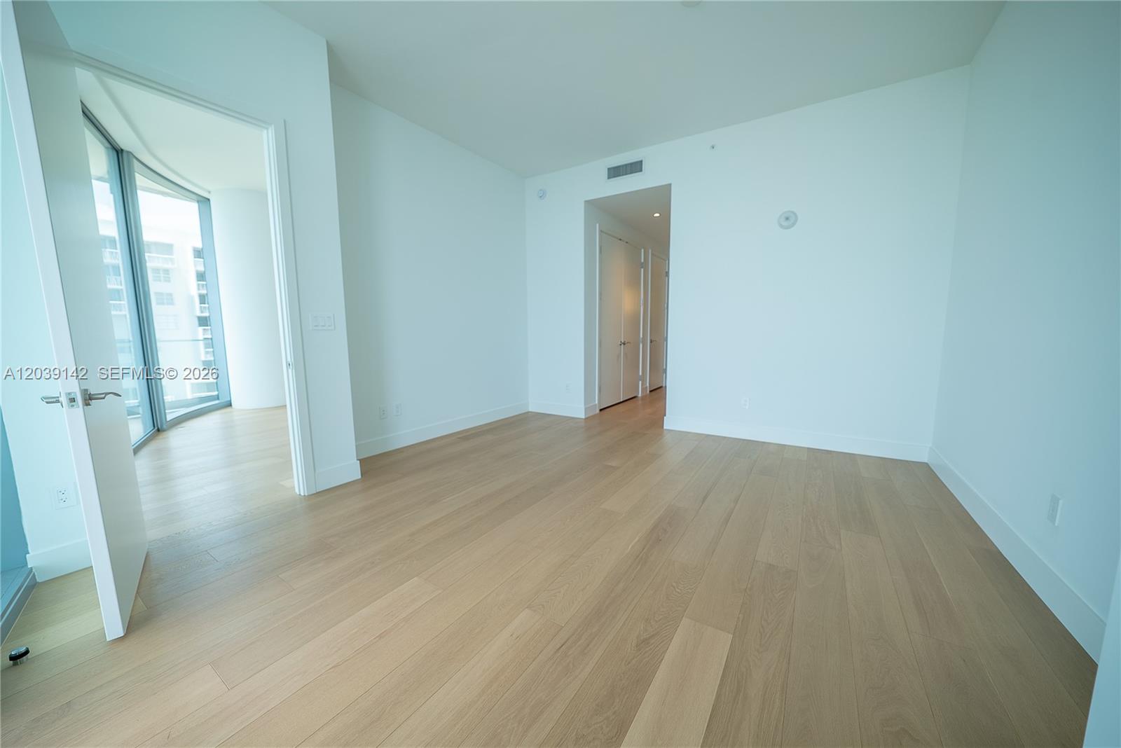An empty room with light wood flooring, white walls, and a doorway leading to a balcony — 175 SE 25th Rd # 702, Miami FL 33129, MIAMI, FL