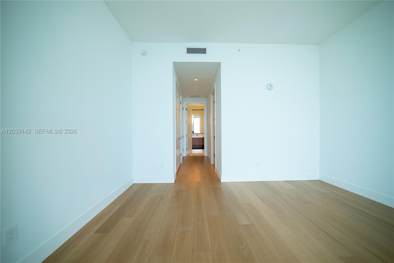 An empty room with light wood flooring leads into a hallway with a bathroom visible — 175 SE 25th Rd # 702, Miami FL 33129, MIAMI, FL