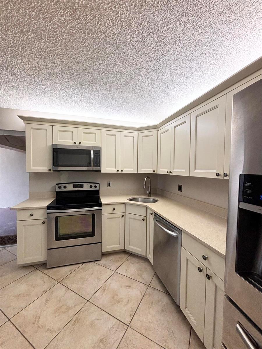 A kitchen features off-white cabinets, stainless steel appliances, beige countertops, and tiled flooring — 203 Foxtail Drive # F1, FL 33415, FL