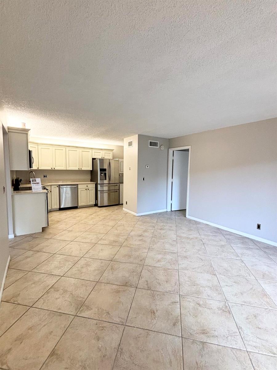 An open-concept kitchen with stainless steel appliances and tile flooring flows into a living area — 203 Foxtail Drive # F1, FL 33415, FL