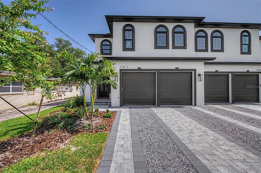A two-story townhouse exterior features a paved driveway, two garage doors, and arched windows — 110 S ARRAWANA AVENUE UNIT 1, TAMPA, FL