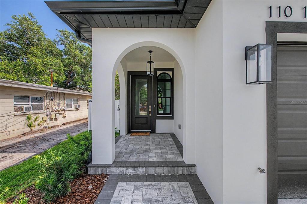 A white stucco house exterior features a covered arched entryway with a paved walkway — 110 S ARRAWANA AVENUE UNIT 1, TAMPA, FL
