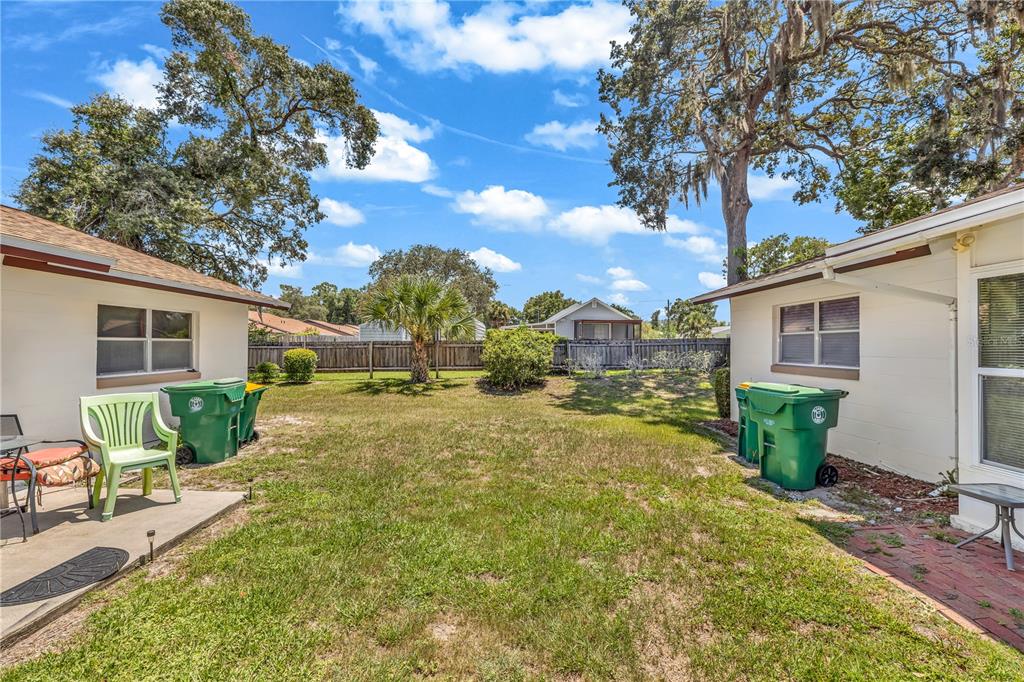 A grassy backyard sits between two single-story residential buildings with green trash bins — 706 E MINNESOTA AVENUE UNIT C, DELAND, FL