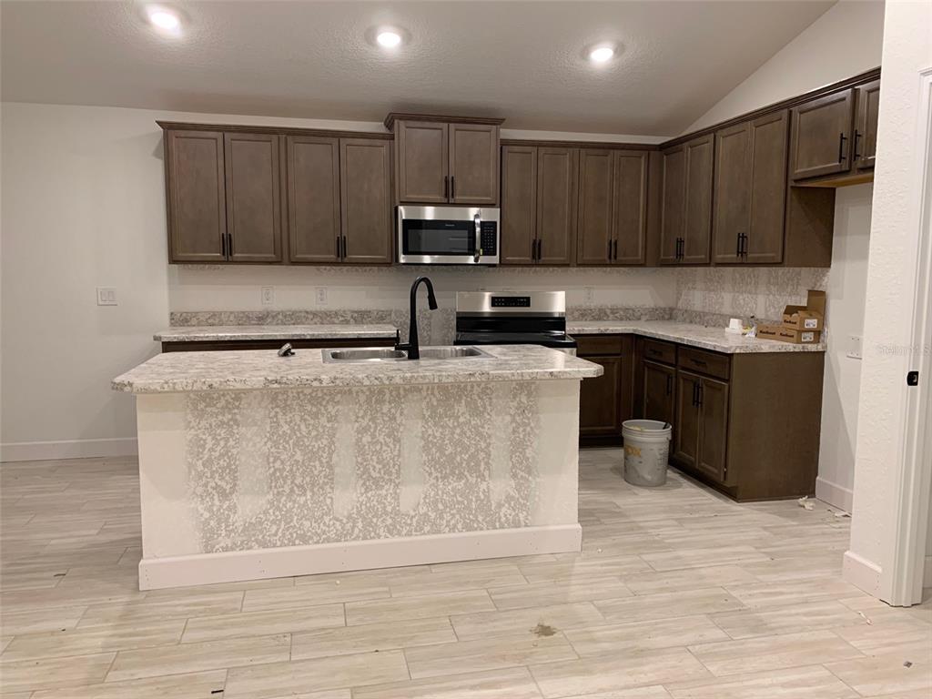 A kitchen features dark wood cabinets, a granite-topped island, and light-colored wood-look tile flooring — 2137 W SAY DRIVE, DUNNELLON, FL
