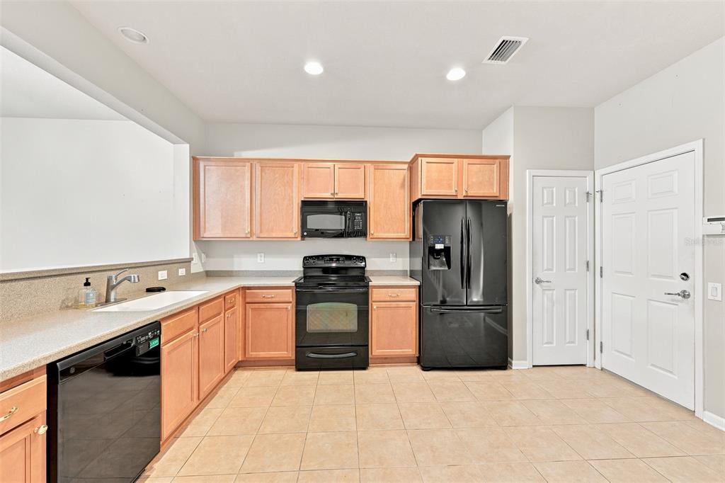 A kitchen features light wood cabinets, black appliances, tile flooring, and a white countertop — 2109 WILD GRAPE PLACE, RIVERVIEW, FL
