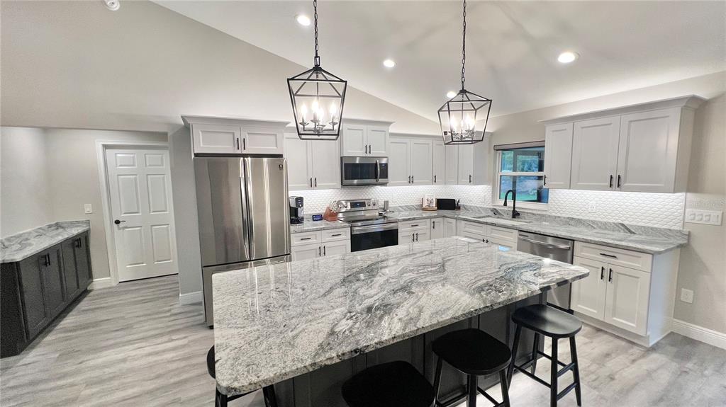A kitchen features light gray cabinets, a large granite island, stainless steel appliances, and pendant lighting — 6944 SW 179TH COURT ROAD, DUNNELLON, FL