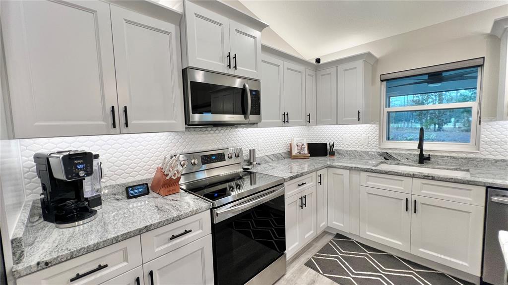 A kitchen features white cabinets, granite countertops, a stainless steel microwave, and a tiled backsplash — 6944 SW 179TH COURT ROAD, DUNNELLON, FL