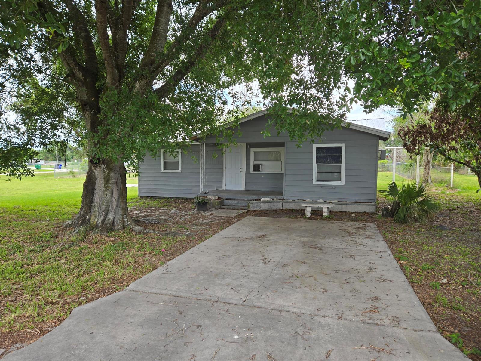 A gray, single-story house with a concrete driveway and a large tree in the yard — 408 NW 10th Avenue, Okeechobee FL 34974, OKEECHOBEE, FL