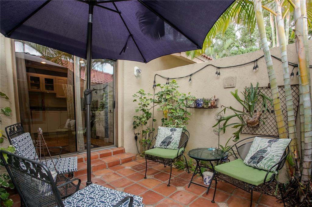 A small patio features terracotta tile flooring, metal furniture, and a large blue umbrella — 1732 KESTRAL PARK WAY S UNIT 43, SARASOTA, FL