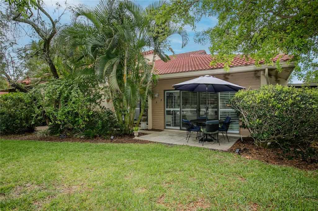 A backyard patio with a dining set and umbrella sits beside a house with siding — 1732 KESTRAL PARK WAY S UNIT 43, SARASOTA, FL
