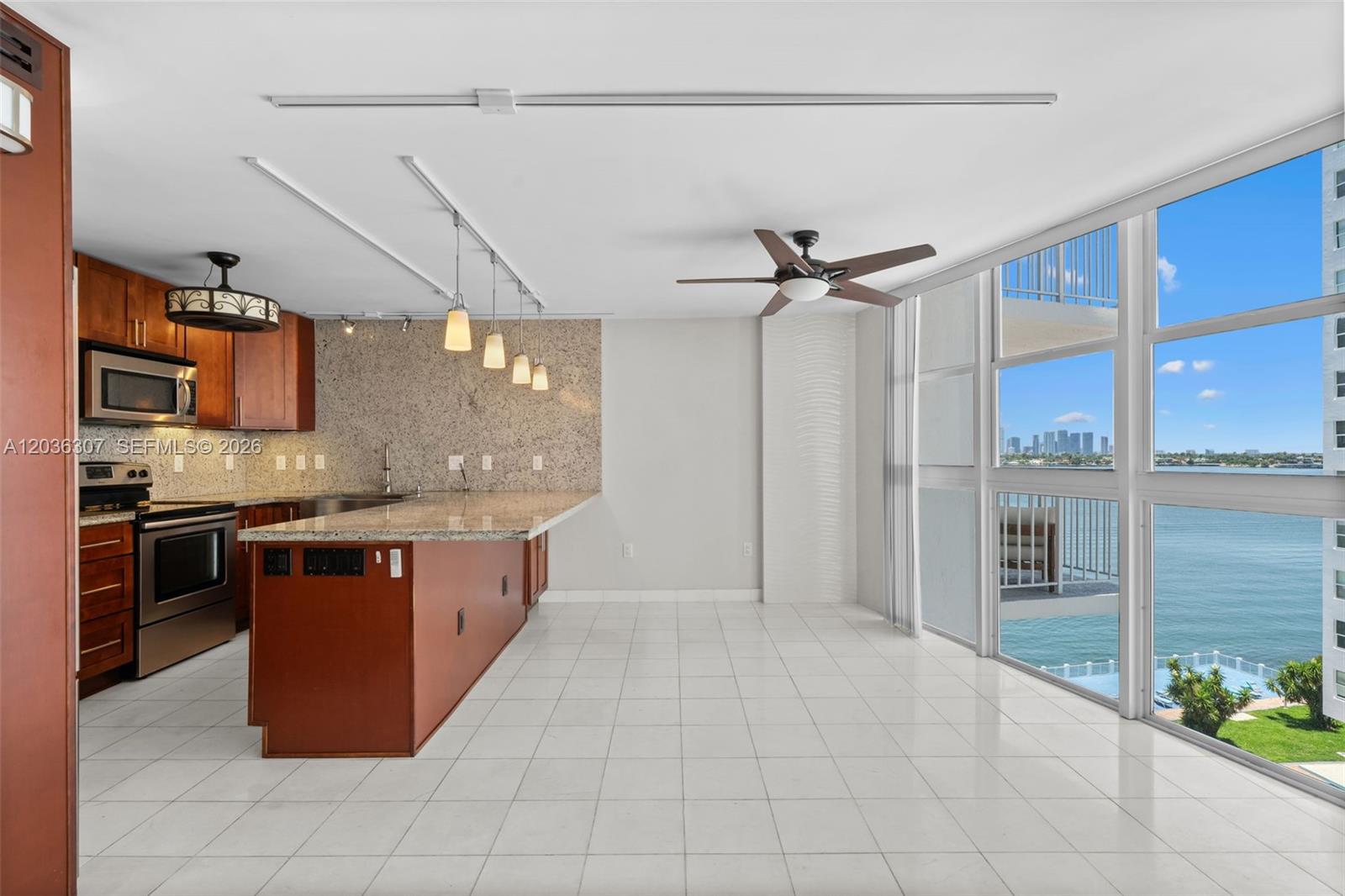 A kitchen with granite countertops and wood cabinets overlooks a balcony and waterfront view — 1228 West Ave # 604, Miami Beach FL 33139, MIAMI BEACH, FL