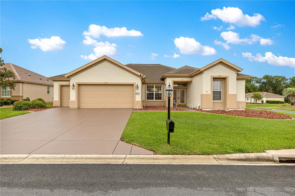 A single-story house with a tan stucco exterior, a two-car garage, and a paved driveway — 9687 SE 137TH STREET ROAD, SUMMERFIELD, FL