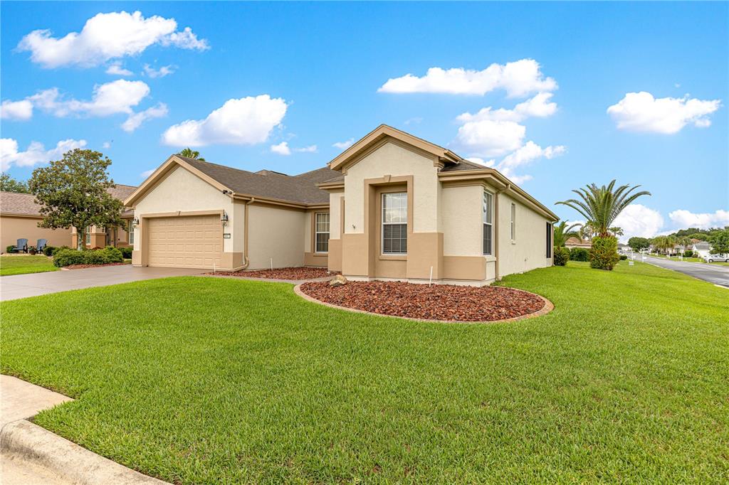 A tan, single-story suburban house with a two-car garage and a landscaped front yard — 9687 SE 137TH STREET ROAD, SUMMERFIELD, FL