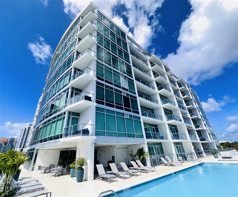 A modern multi-story apartment building with glass balconies overlooks an outdoor swimming pool — 101 S EOLA DRIVE UNIT 1203, ORLANDO, FL