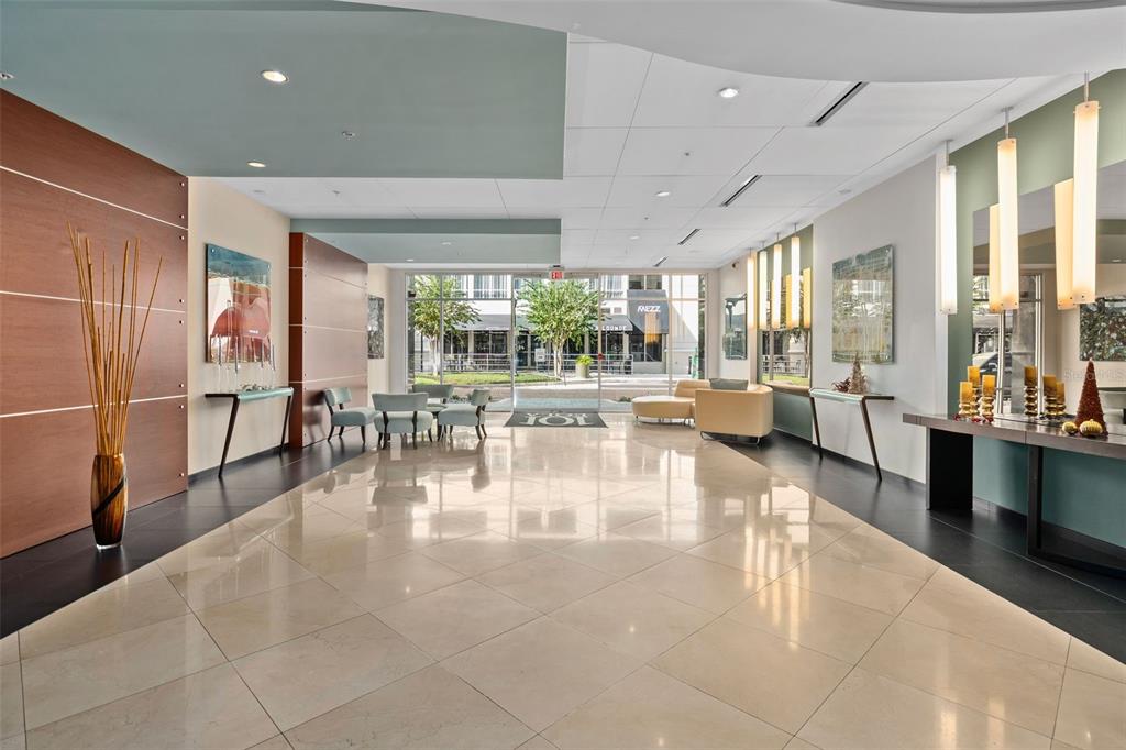 A modern building lobby features polished tile floors, wood paneling, and floor-to-ceiling glass doors — 101 S EOLA DRIVE UNIT 1203, ORLANDO, FL