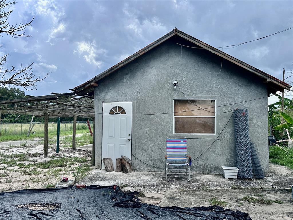 A small, stucco-finished building with a white door, a single window, and an attached trellis — 802 SCENIC HIGHWAY N, LAKE HAMILTON, FL
