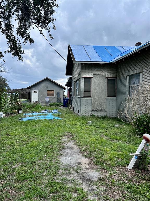 A brick house with a blue tarp roof stands next to a small detached building — 802 SCENIC HIGHWAY N, LAKE HAMILTON, FL