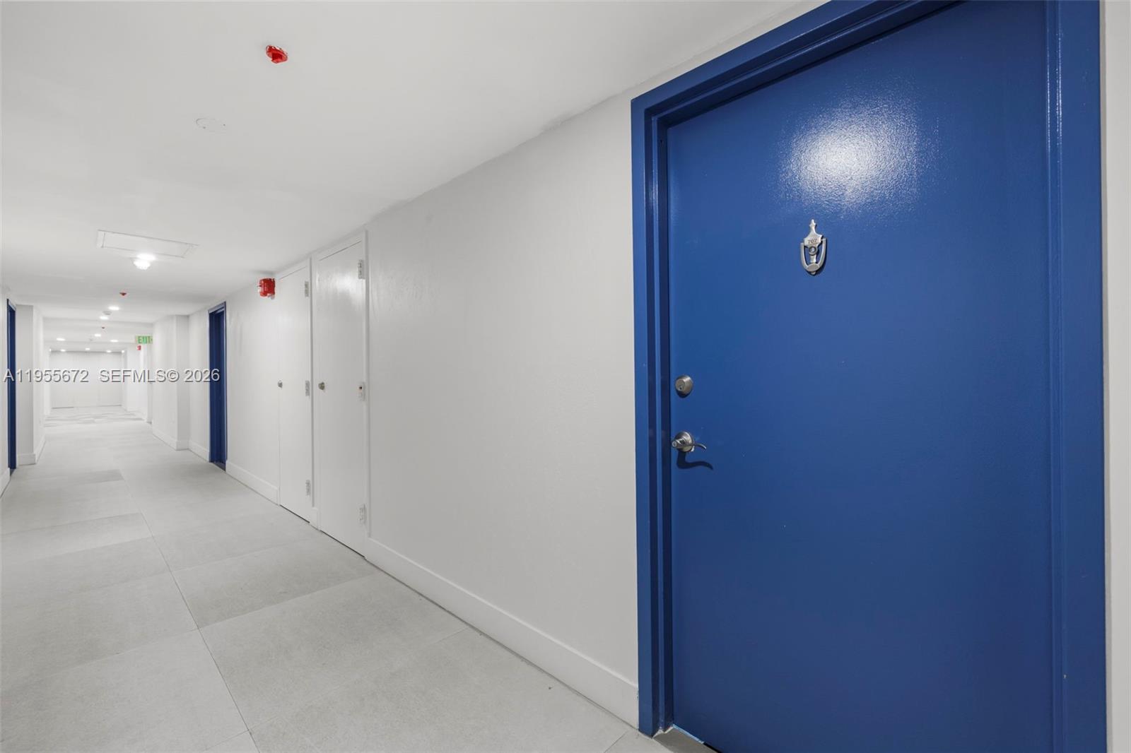 A bright hallway features a blue door, white walls, and light-colored tiled flooring — 2655 Collins Ave # 707, Miami Beach FL 33140, MIAMI BEACH, FL