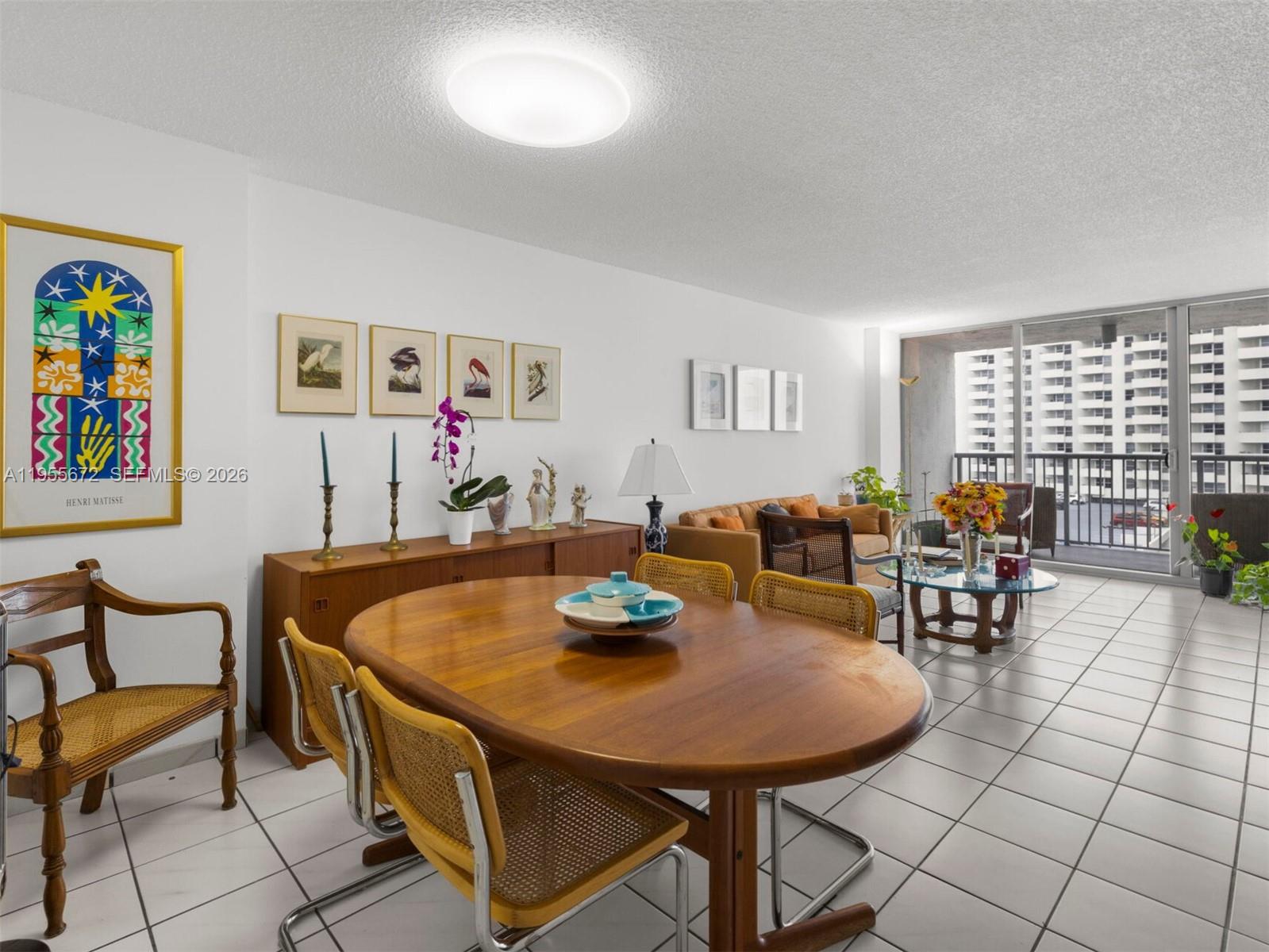 A dining and living area features a wooden table, tile flooring, and a balcony view — 2655 Collins Ave # 707, Miami Beach FL 33140, MIAMI BEACH, FL