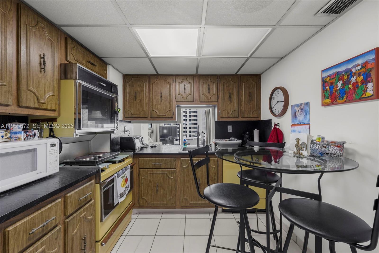 A kitchen features wood cabinets, yellow appliances, a glass-top table, and a drop ceiling — 2655 Collins Ave # 707, Miami Beach FL 33140, MIAMI BEACH, FL