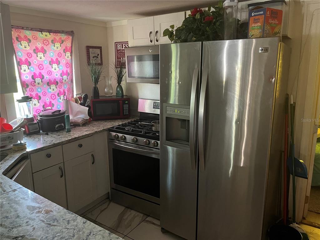 A kitchen features stainless steel appliances, white cabinets, and a window with Minnie Mouse curtains — 1161 KINGSLEY STREET, CLEARWATER, FL
