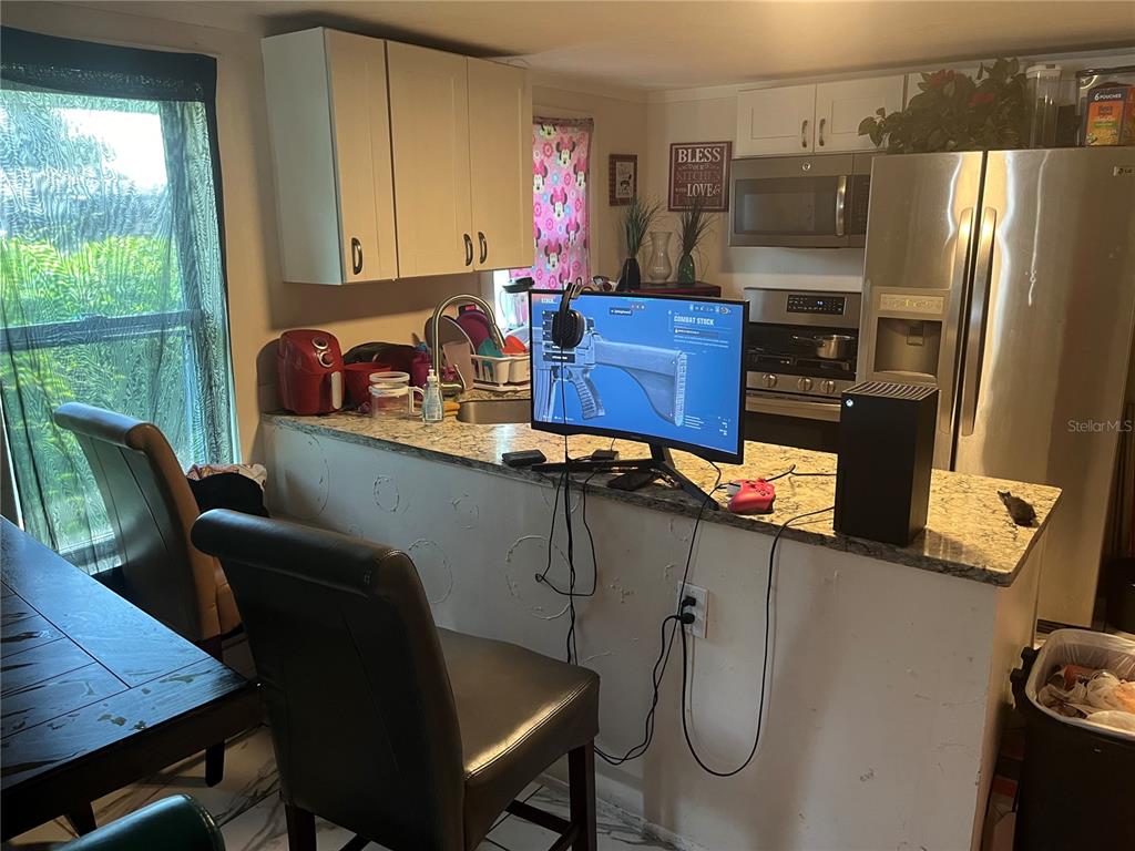 A kitchen features a granite-topped island with a gaming monitor and console setup — 1161 KINGSLEY STREET, CLEARWATER, FL