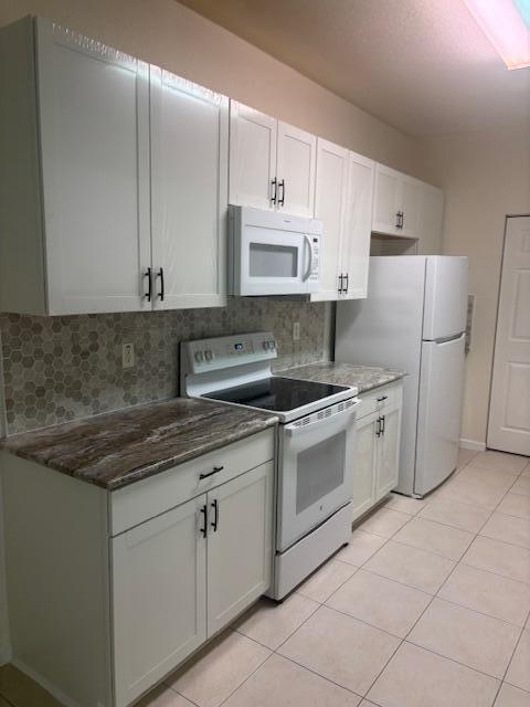 A kitchen features white cabinets, a white microwave and stove, and a patterned stone countertop — 3557 Forest Hill Boulevard # 49, Palm Springs FL 33406, PALM SPRINGS, FL
