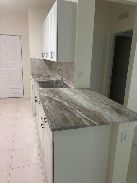 A kitchen features white cabinets, a patterned backsplash, and a brown and white stone countertop — 3557 Forest Hill Boulevard # 49, Palm Springs FL 33406, PALM SPRINGS, FL