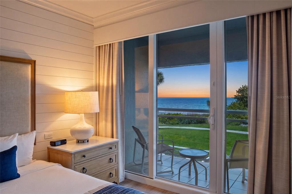 A bedroom with white shiplap walls features a bedside lamp and sliding doors overlooking the ocean — 240 SANDS POINT ROAD UNIT 4104, LONGBOAT KEY, FL