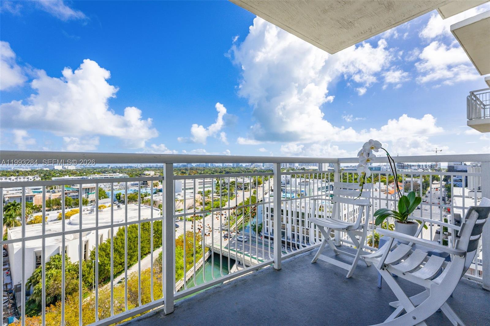 A balcony with white chairs and a potted orchid overlooks a city canal and street — 1688 West Ave # 1205, Miami Beach FL 33139, MIAMI BEACH, FL