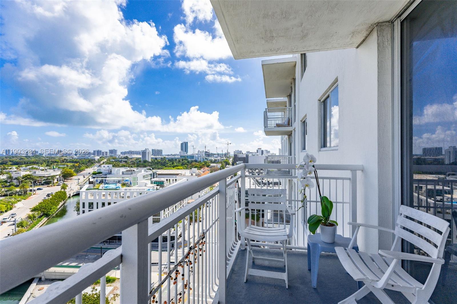 A balcony with white chairs and a potted orchid overlooks a city and canal — 1688 West Ave # 1205, Miami Beach FL 33139, MIAMI BEACH, FL