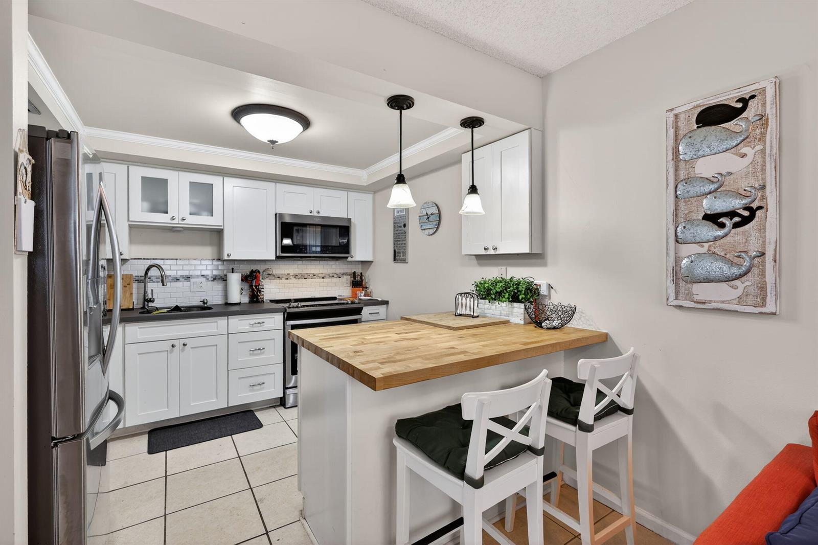 A kitchen features white cabinets, a butcher block island with two chairs, and tile flooring — 950 S Kanner Highway # 603, Stuart FL 34994, STUART, FL