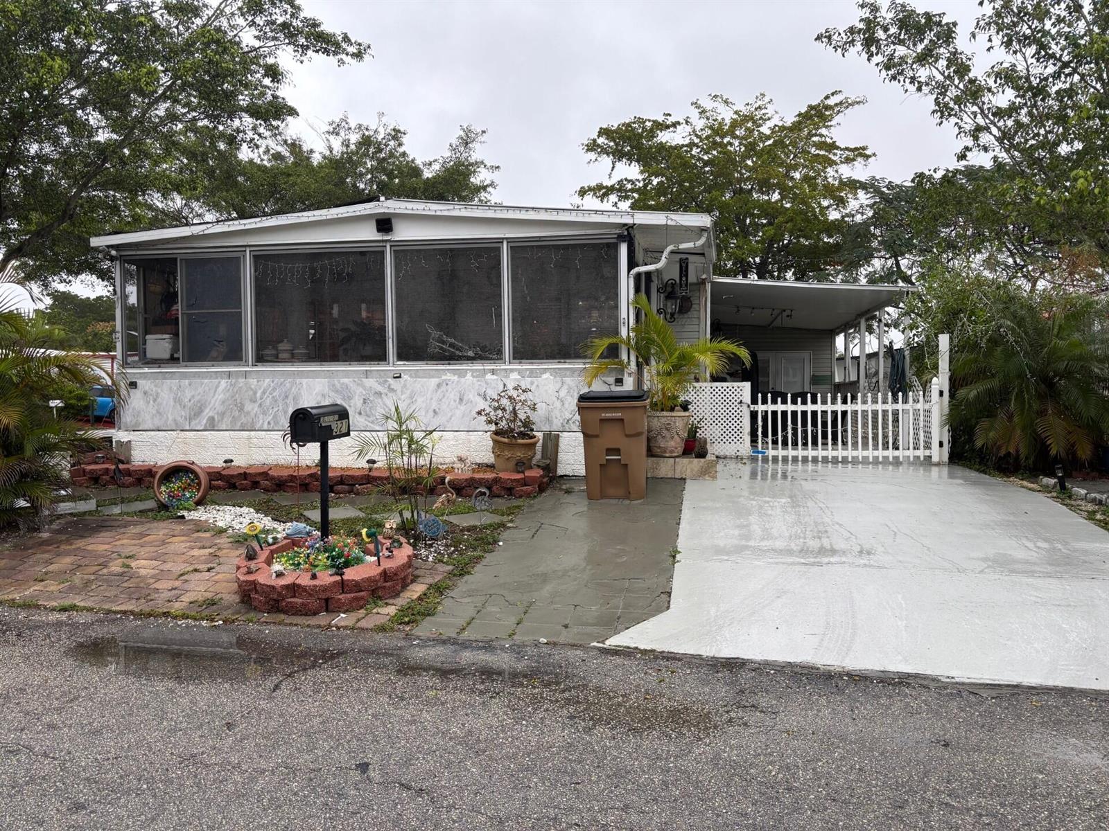 A single-story manufactured home with a screened-in porch, paved driveway, and a white picket fence — 321 NW 48th Court, Pompano Beach FL 33064, POMPANO BEACH, FL