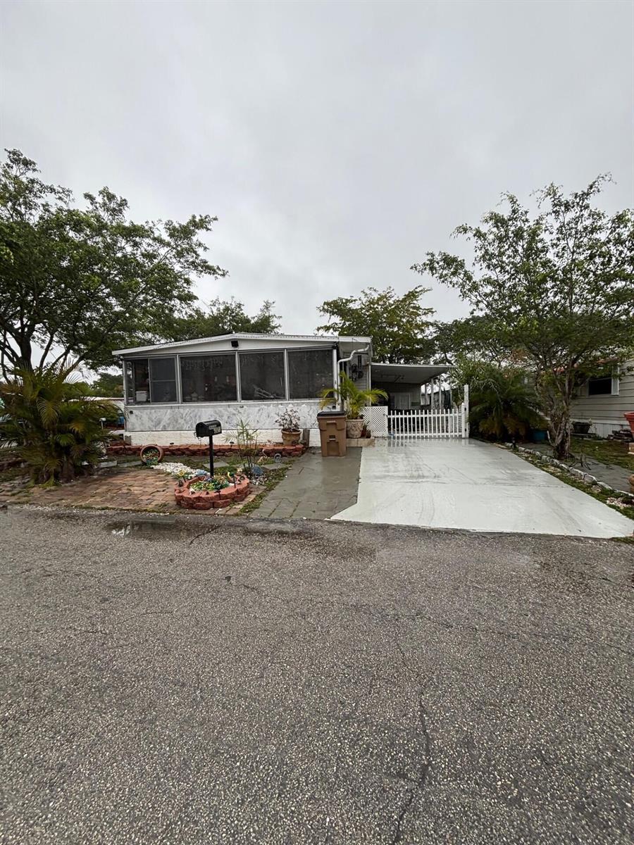 A single-story manufactured home features a screened-in porch, a paved driveway, and a white fence — 321 NW 48th Court, Pompano Beach FL 33064, POMPANO BEACH, FL