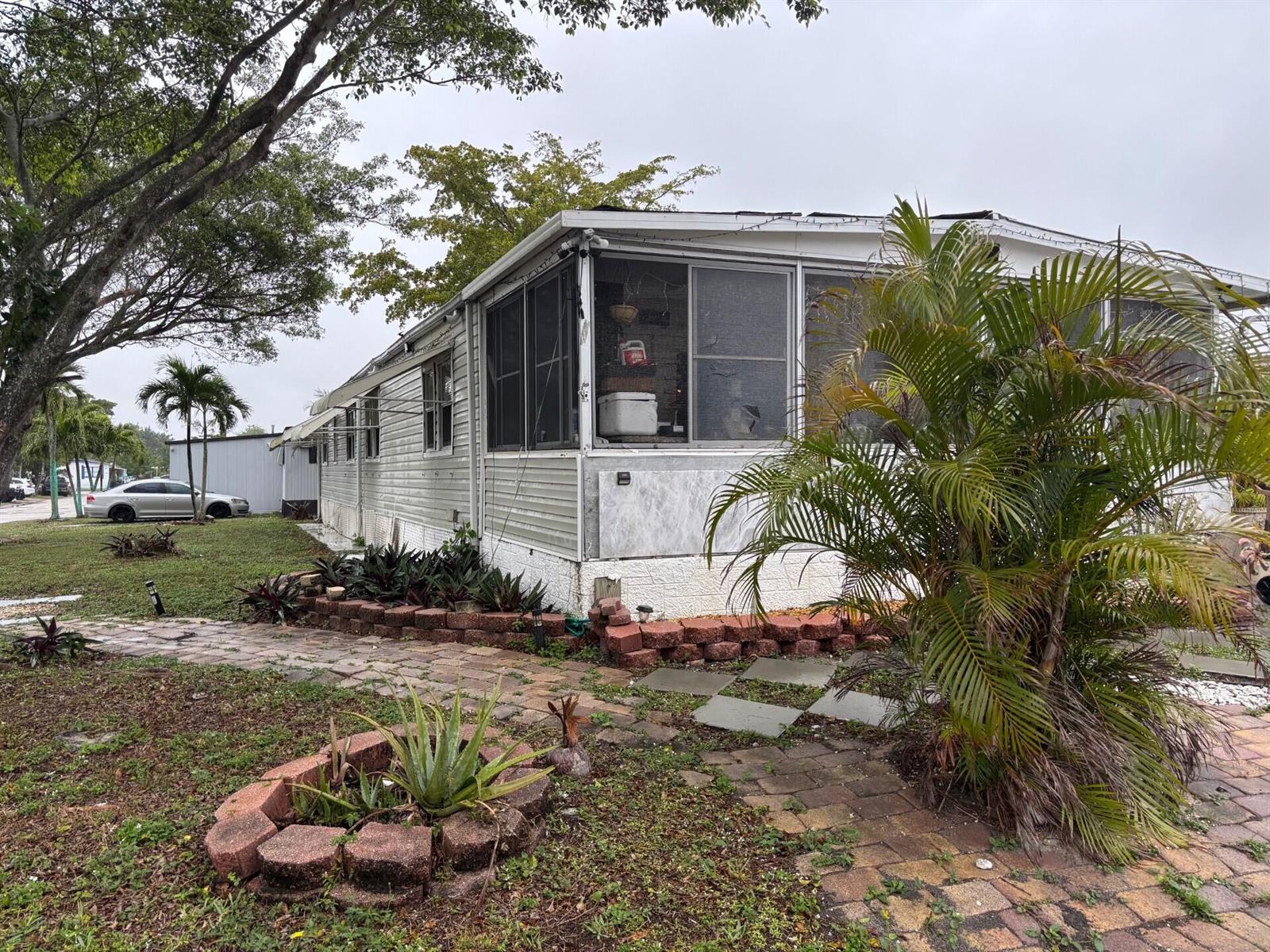 A single-story mobile home with a screened-in porch, brick landscaping borders, and palm trees — 321 NW 48th Court, Pompano Beach FL 33064, POMPANO BEACH, FL