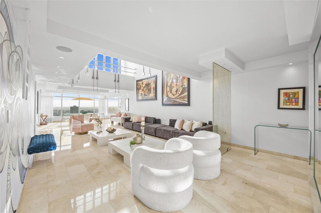 A bright, modern living room features white textured armchairs, a long sofa, and marble floors — 14 RD 833, LA CIMA UNIT PH 1901, GUAYNABO, PR
