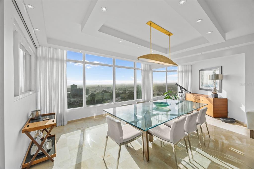 A bright dining room features a glass table, modern chairs, and floor-to-ceiling windows with views — 14 RD 833, LA CIMA UNIT PH 1901, GUAYNABO, PR