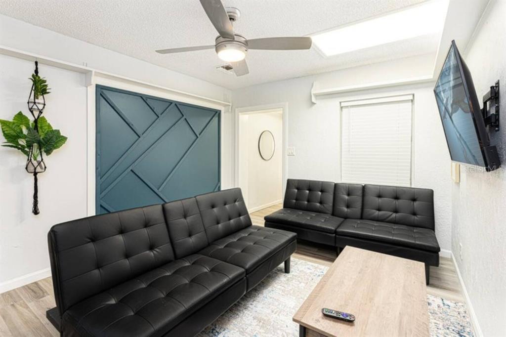 A living room features two black futons, a wood coffee table, and a blue accent wall — 1214 N PINE HILLS ROAD, ORLANDO, FL