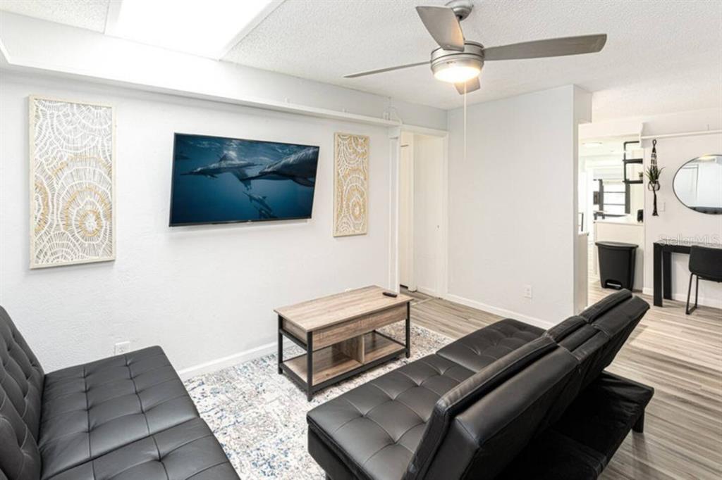 A living room features two black futons, a wood coffee table, and a wall-mounted television — 1214 N PINE HILLS ROAD, ORLANDO, FL