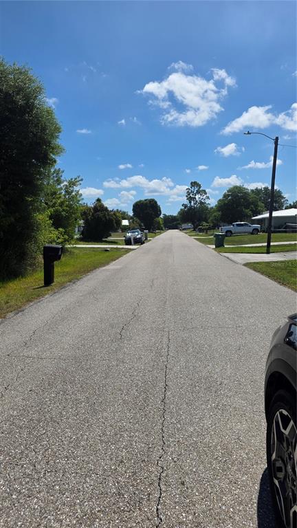 A paved residential street stretches into the distance under a bright, partly cloudy sky — 22344 BUFFALO AVENUE, PORT CHARLOTTE, FL