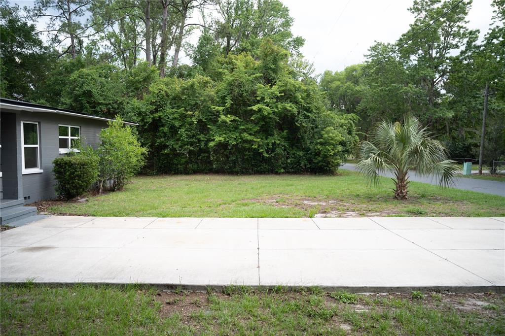 A concrete driveway leads to a grassy yard beside a gray house with two windows — 1015 SE 10TH TERRACE, GAINESVILLE, FL