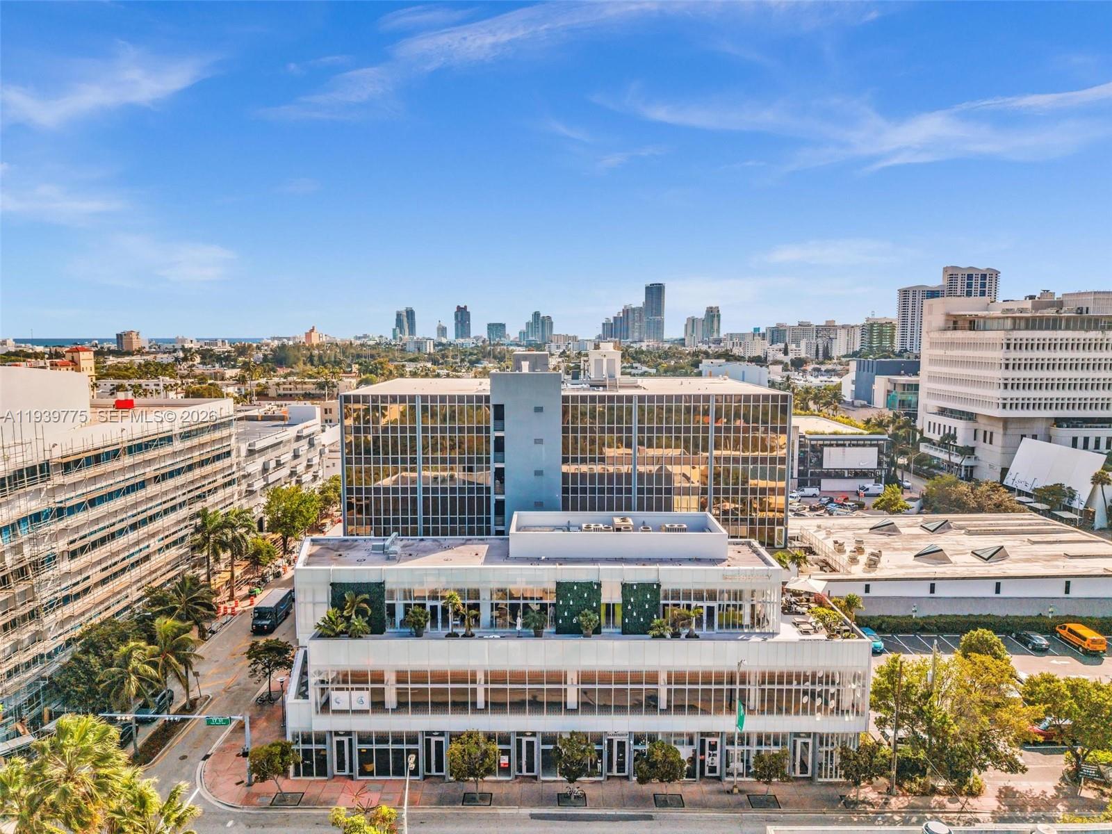 An aerial view shows a modern white commercial building with a glass-paneled office tower behind — 1680 Michigan Ave, Miami Beach FL 33139, MIAMI BEACH, FL