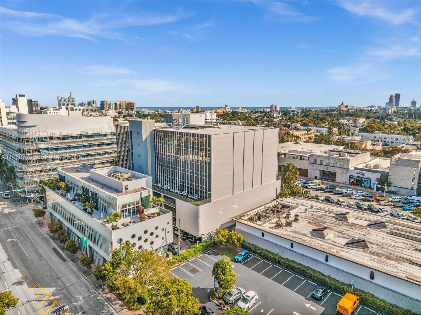 An aerial view shows a modern office building with a parking lot and surrounding city — 1680 Michigan Ave, Miami Beach FL 33139, MIAMI BEACH, FL