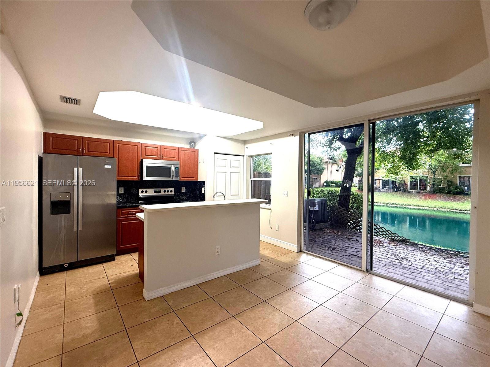 A kitchen with wood cabinets and stainless steel appliances overlooks a patio and lake — 4932 Windward Way # 1301, Dania Beach FL 33312, DANIA BEACH, FL