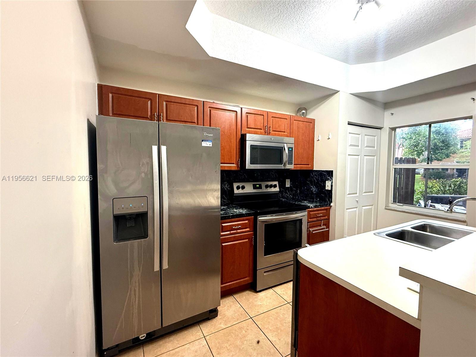 A kitchen features stainless steel appliances, wood cabinets, dark countertops, and a double sink — 4932 Windward Way # 1301, Dania Beach FL 33312, DANIA BEACH, FL