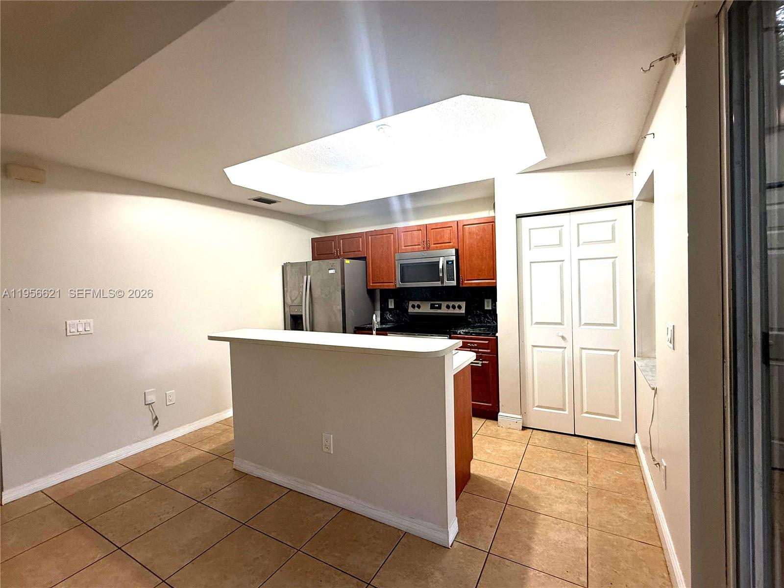 A kitchen features a breakfast bar, wooden cabinets, stainless steel appliances, and tile flooring — 4932 Windward Way # 1301, Dania Beach FL 33312, DANIA BEACH, FL