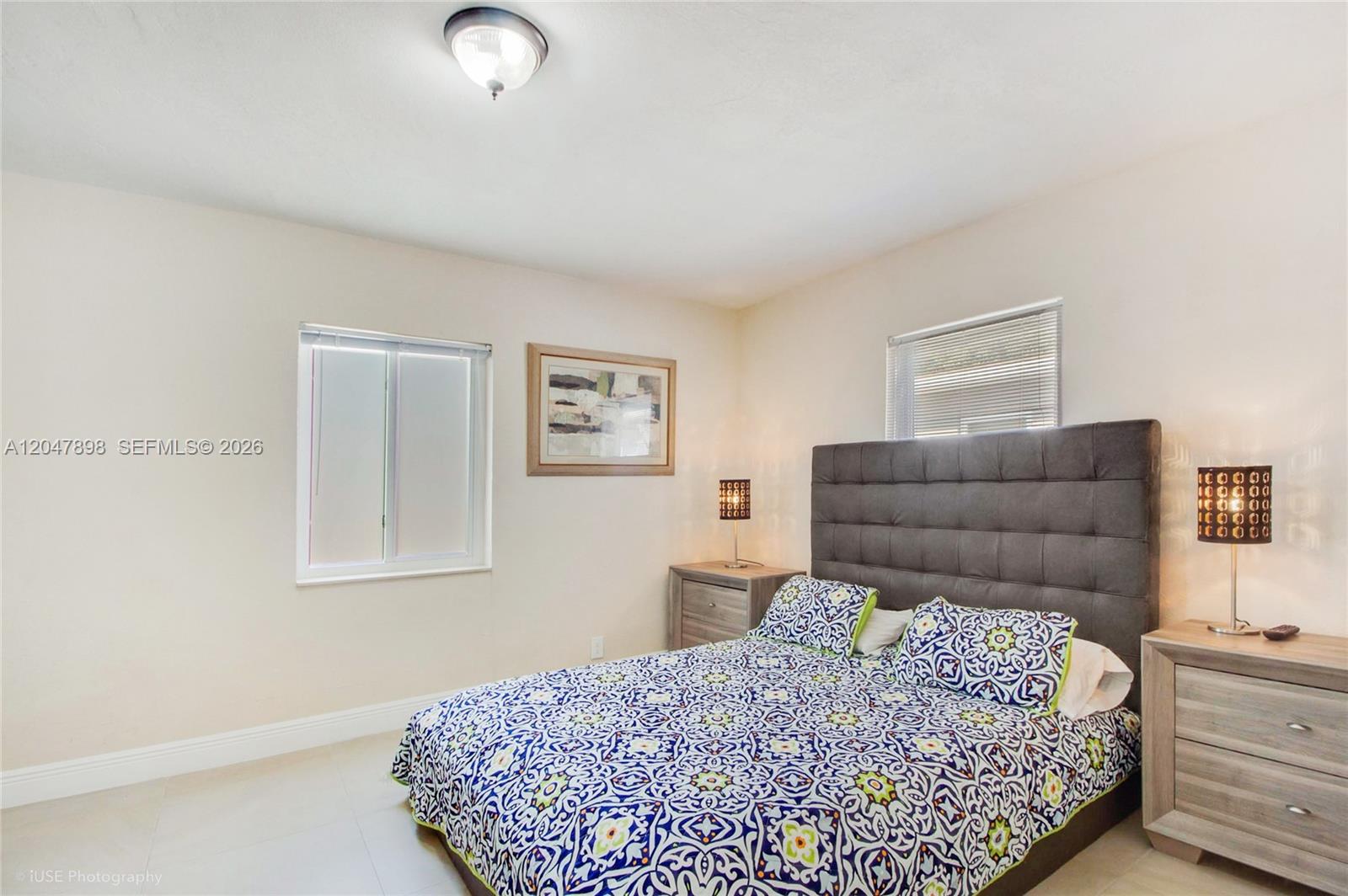 A bedroom features a tufted gray headboard, patterned bedding, two nightstands, and two windows — 518 SW 7th Ave # 520, Miami FL 33130, MIAMI, FL
