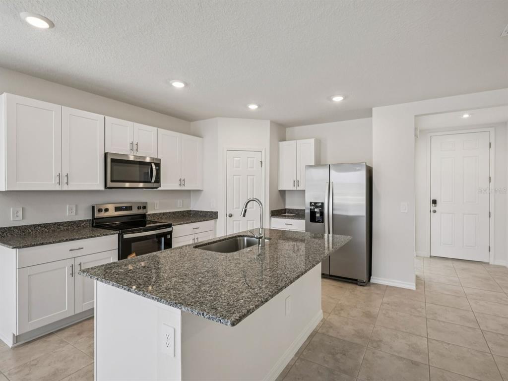 A kitchen features white cabinets, granite countertops, stainless steel appliances, and a central island — 3865 GIORGIO DRIVE, WINTER HAVEN, FL