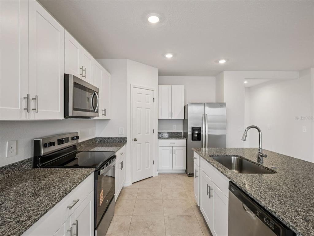 A kitchen features white cabinets, granite countertops, stainless steel appliances, and tile flooring — 3865 GIORGIO DRIVE, WINTER HAVEN, FL